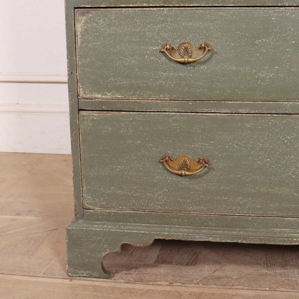 A distressed sage green painted wooden chest of drawers featuring two short over three long drawers with decorative brass handles and bracket feet. View V
