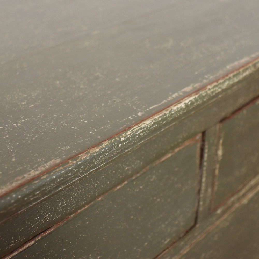 A distressed sage green painted wooden chest of drawers featuring two short over three long drawers with decorative brass handles and bracket feet. View X