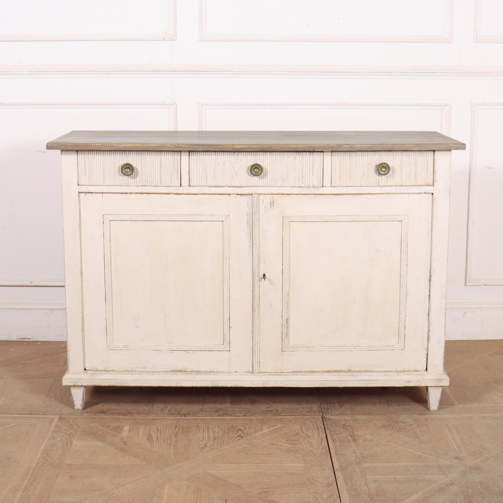 An off-white painted Continental wooden buffet featuring three reeded top drawers with round brass knobs above two large panelled cupboard doors and a grey painted top surface.