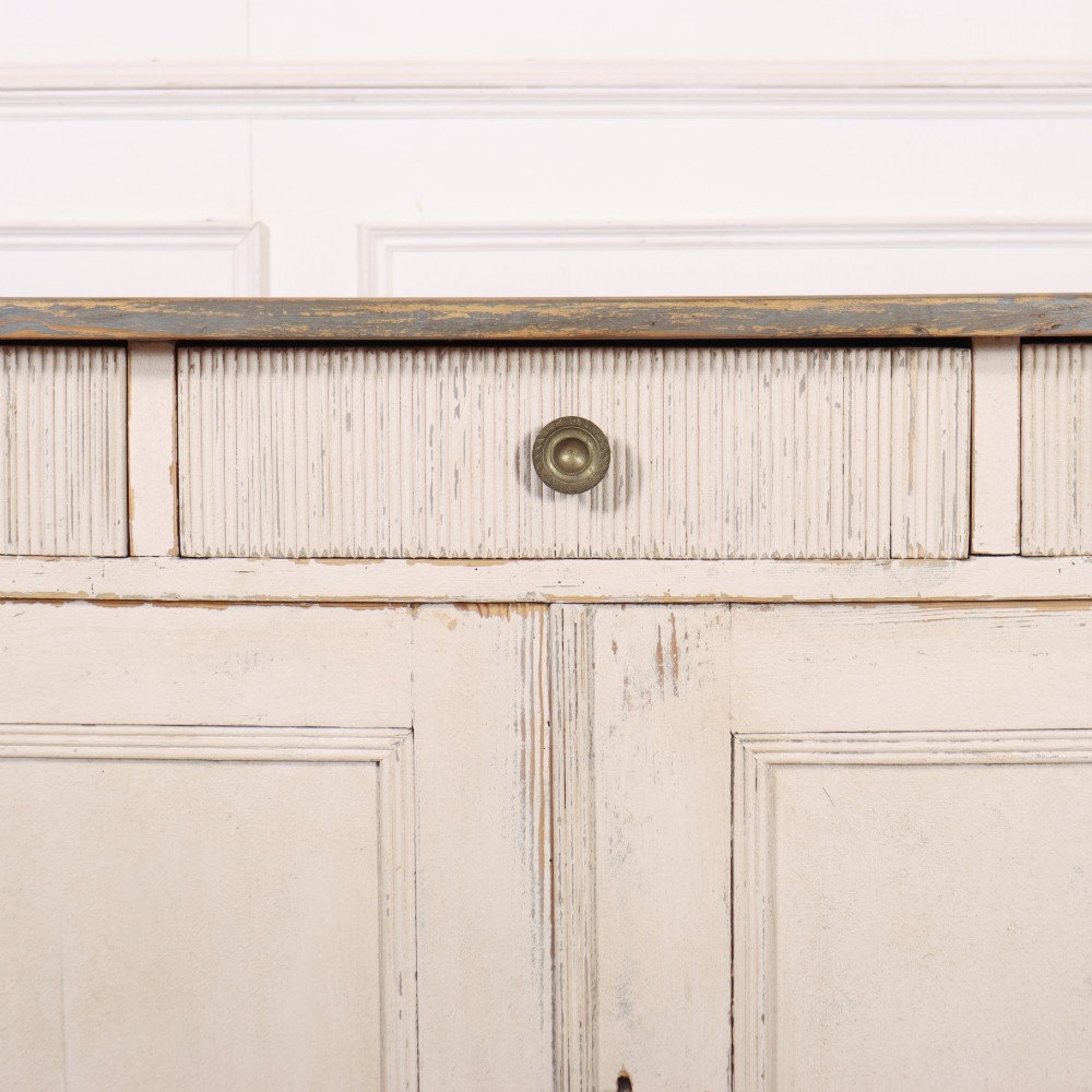 An off-white painted Continental wooden buffet featuring three reeded top drawers with round brass knobs above two large panelled cupboard doors and a grey painted top surface. View III