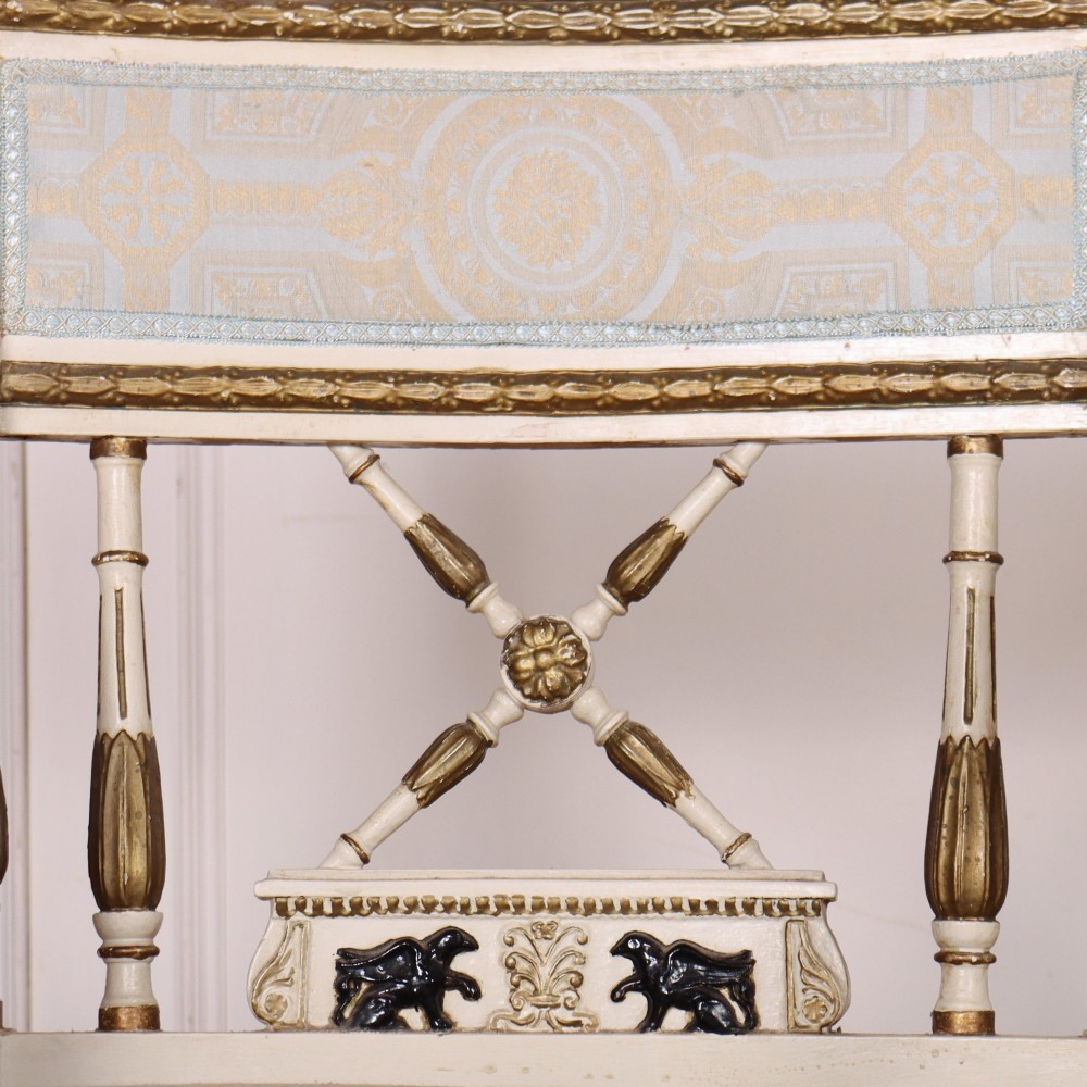 A pair of Swedish Empire style armchairs with pale cream and gilt painted frames, X-back spindle details, and light blue patterned fabric upholstery. View VI