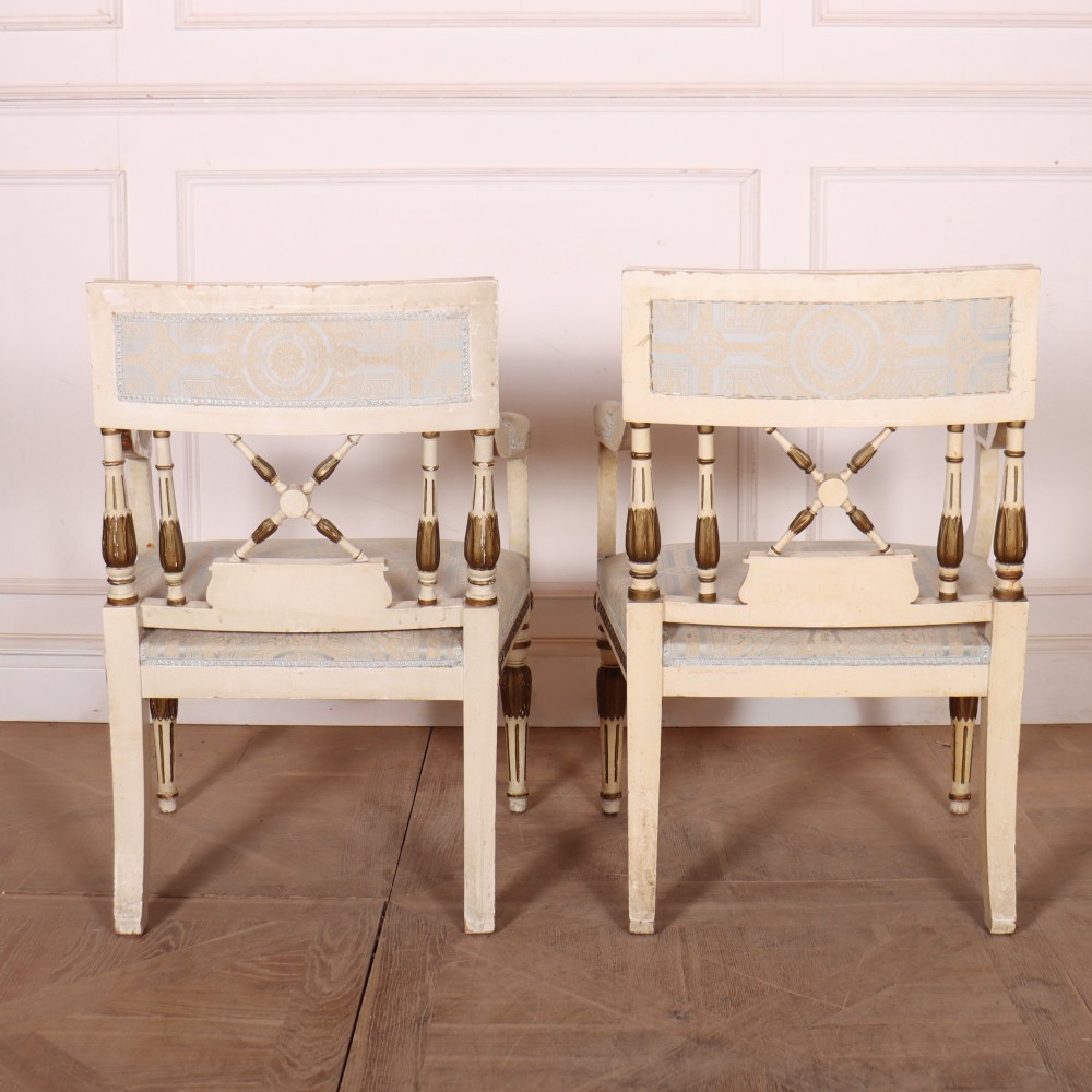 A pair of Swedish Empire style armchairs with pale cream and gilt painted frames, X-back spindle details, and light blue patterned fabric upholstery. View X
