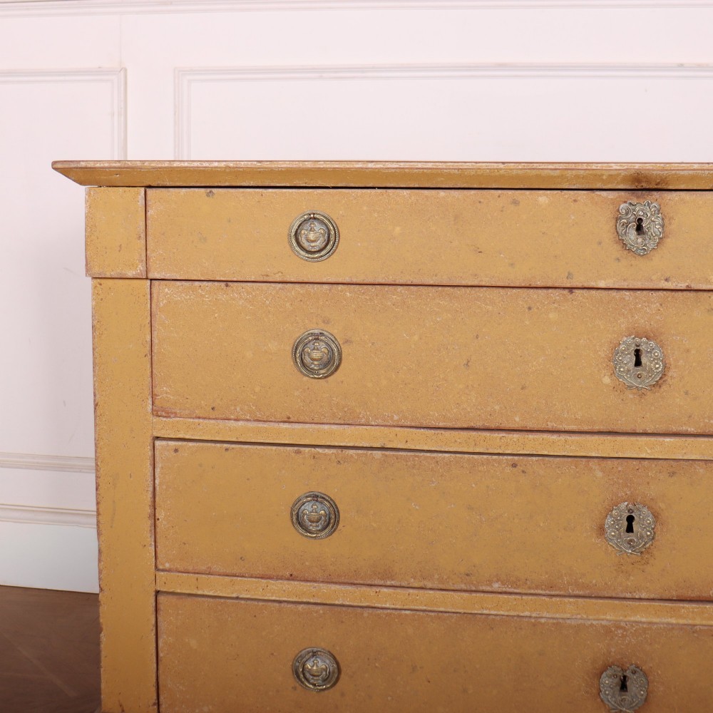 An antique French four-drawer wooden commode featuring an ochre painted finish with brass ring pull handles and central keyhole escutcheons. View II