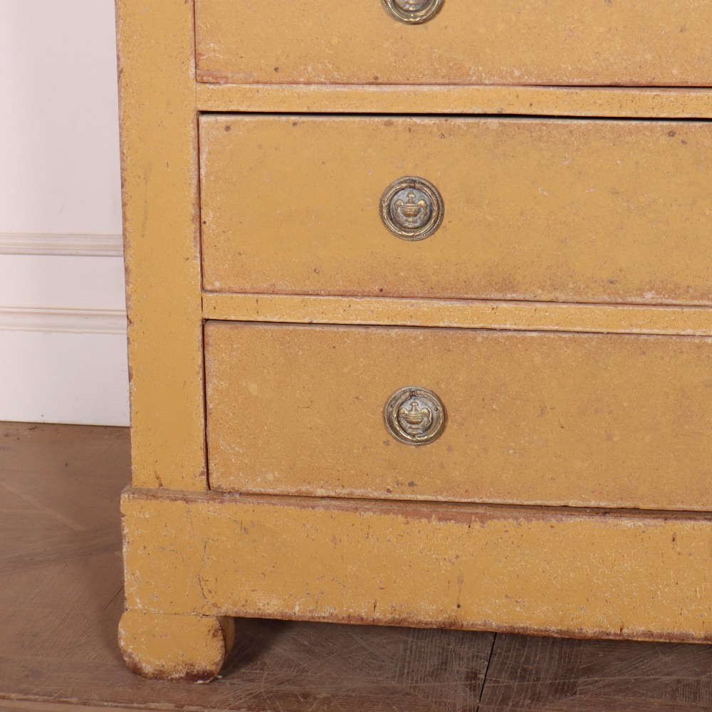 An antique French four-drawer wooden commode featuring an ochre painted finish with brass ring pull handles and central keyhole escutcheons. View V