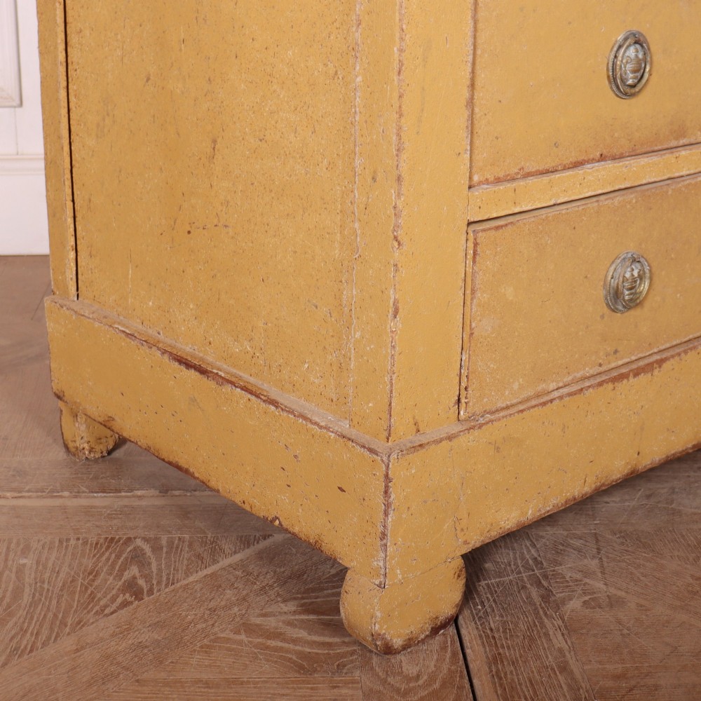 An antique French four-drawer wooden commode featuring an ochre painted finish with brass ring pull handles and central keyhole escutcheons. View X
