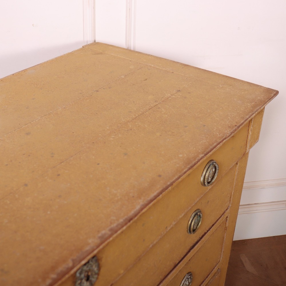 An antique French four-drawer wooden commode featuring an ochre painted finish with brass ring pull handles and central keyhole escutcheons. View XII