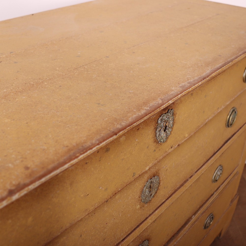An antique French four-drawer wooden commode featuring an ochre painted finish with brass ring pull handles and central keyhole escutcheons. View XIII