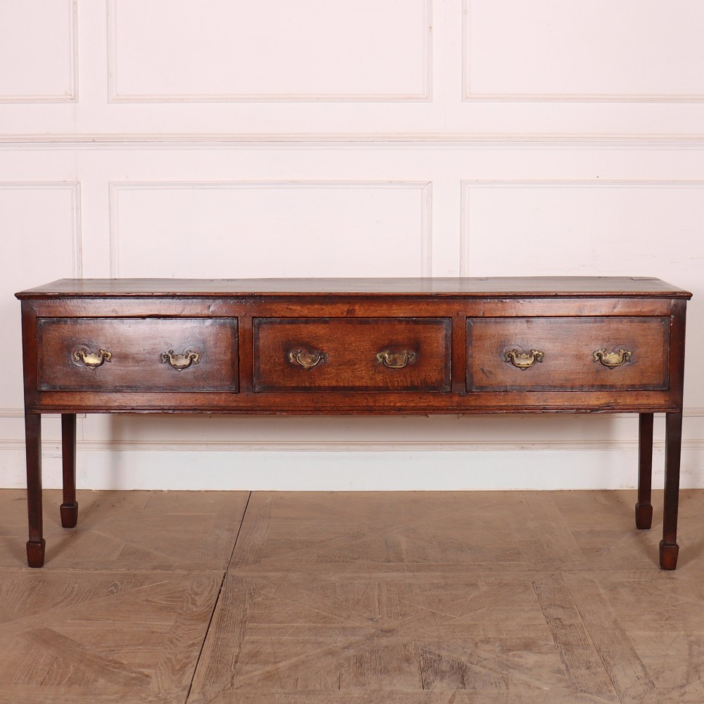 An eighteenth-century English oak dresser base featuring three drawers with brass swan-neck handles, raised on four slender straight legs.