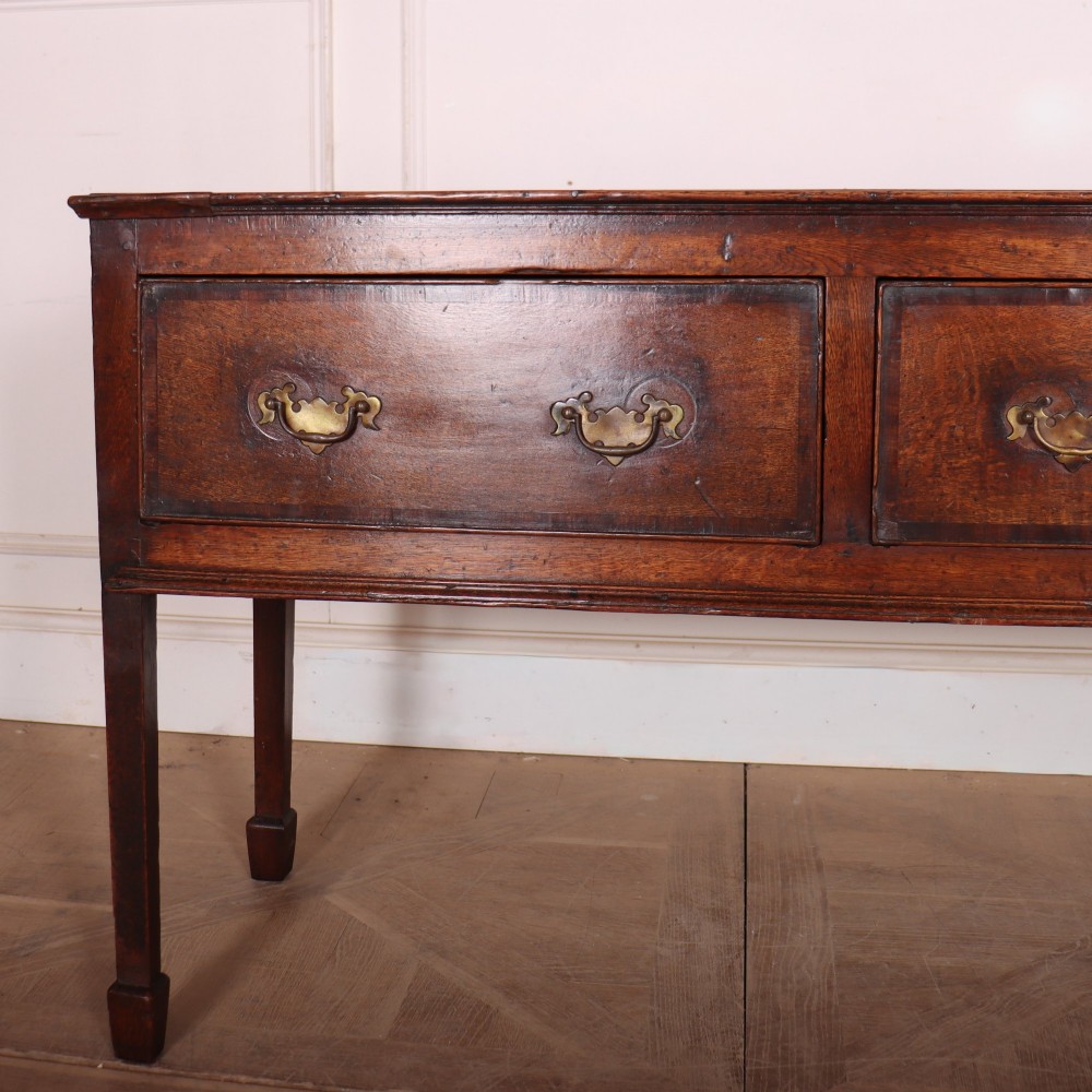An eighteenth-century English oak dresser base featuring three drawers with brass swan-neck handles, raised on four slender straight legs. View II