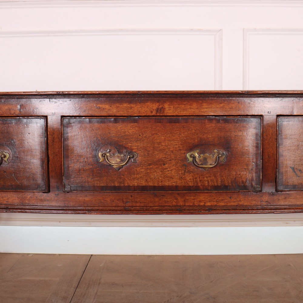 An eighteenth-century English oak dresser base featuring three drawers with brass swan-neck handles, raised on four slender straight legs. View III