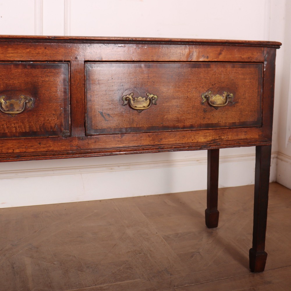 An eighteenth-century English oak dresser base featuring three drawers with brass swan-neck handles, raised on four slender straight legs. View IV