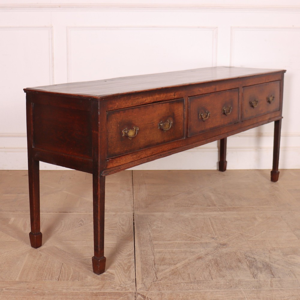 An eighteenth-century English oak dresser base featuring three drawers with brass swan-neck handles, raised on four slender straight legs. View VI