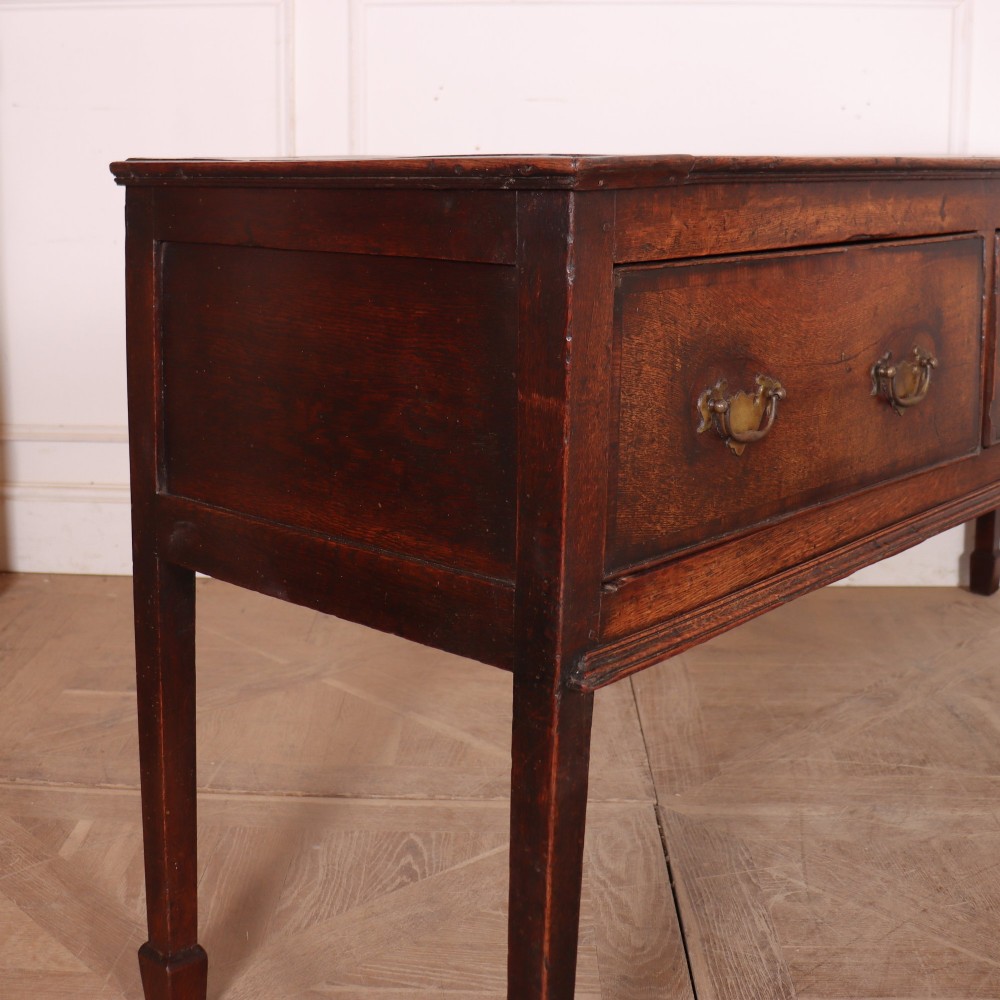 An eighteenth-century English oak dresser base featuring three drawers with brass swan-neck handles, raised on four slender straight legs. View VII