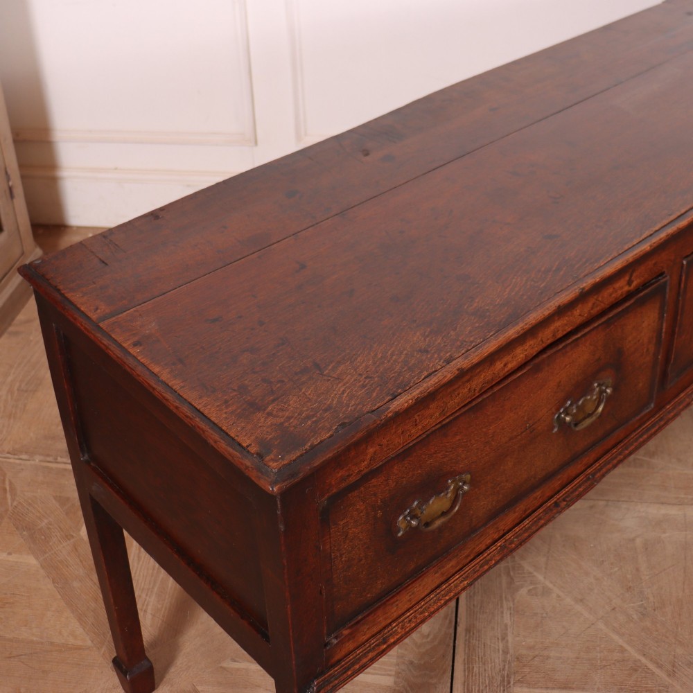 An eighteenth-century English oak dresser base featuring three drawers with brass swan-neck handles, raised on four slender straight legs. View IX