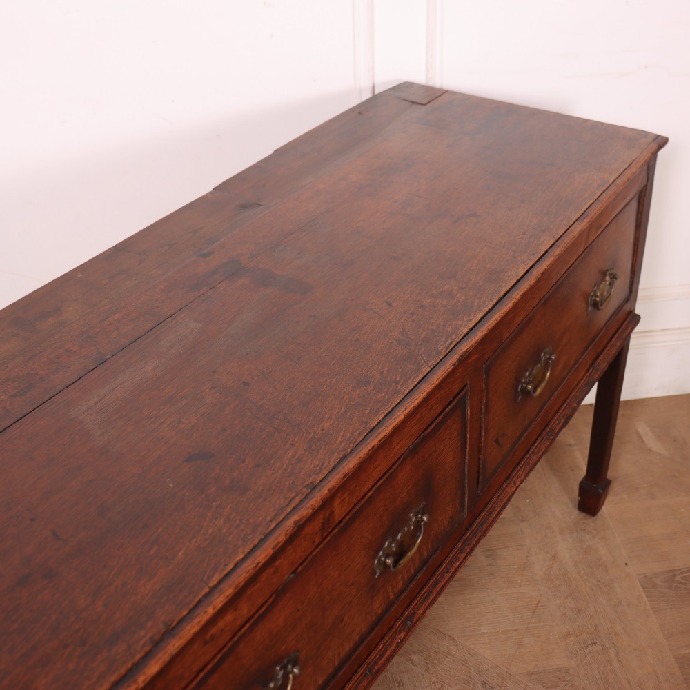 An eighteenth-century English oak dresser base featuring three drawers with brass swan-neck handles, raised on four slender straight legs. View X
