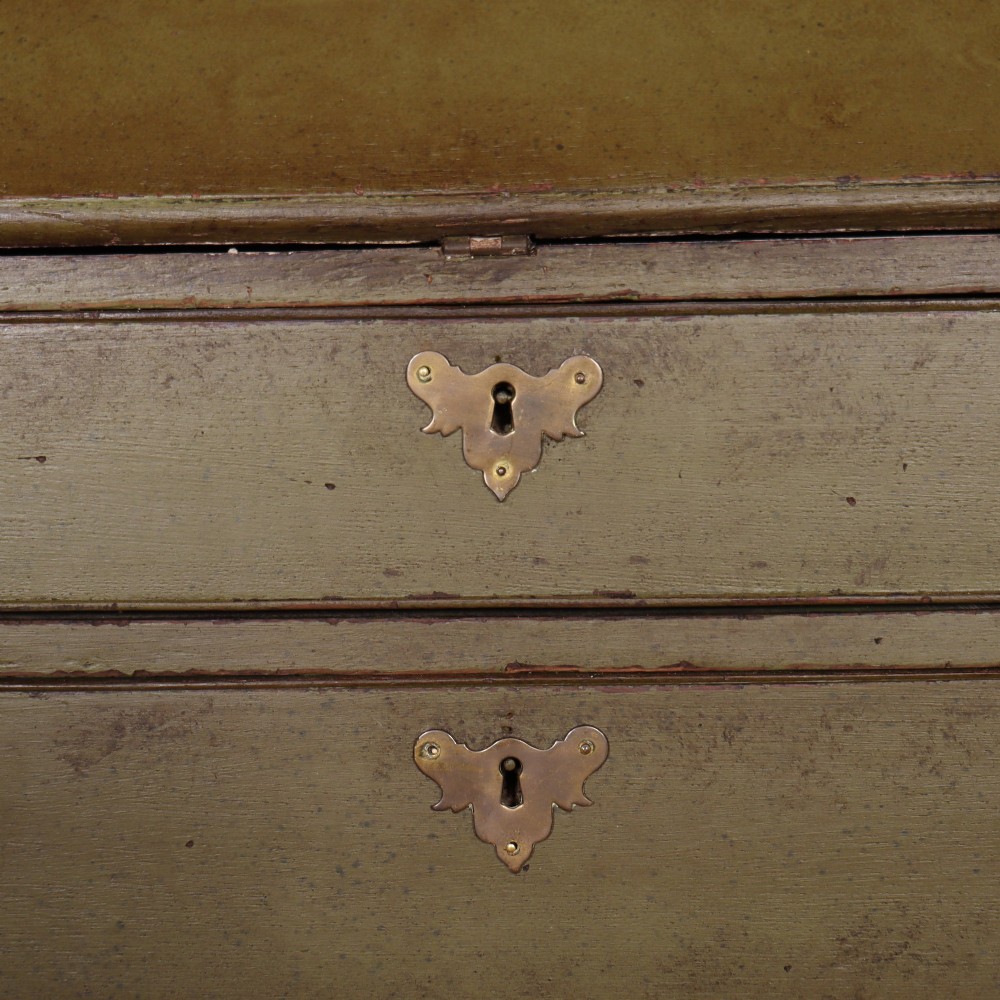 An antique English slant-front bureau with an olive green painted finish, brass handles, keyhole escutcheons, and four drawers resting on bracket feet. View VI