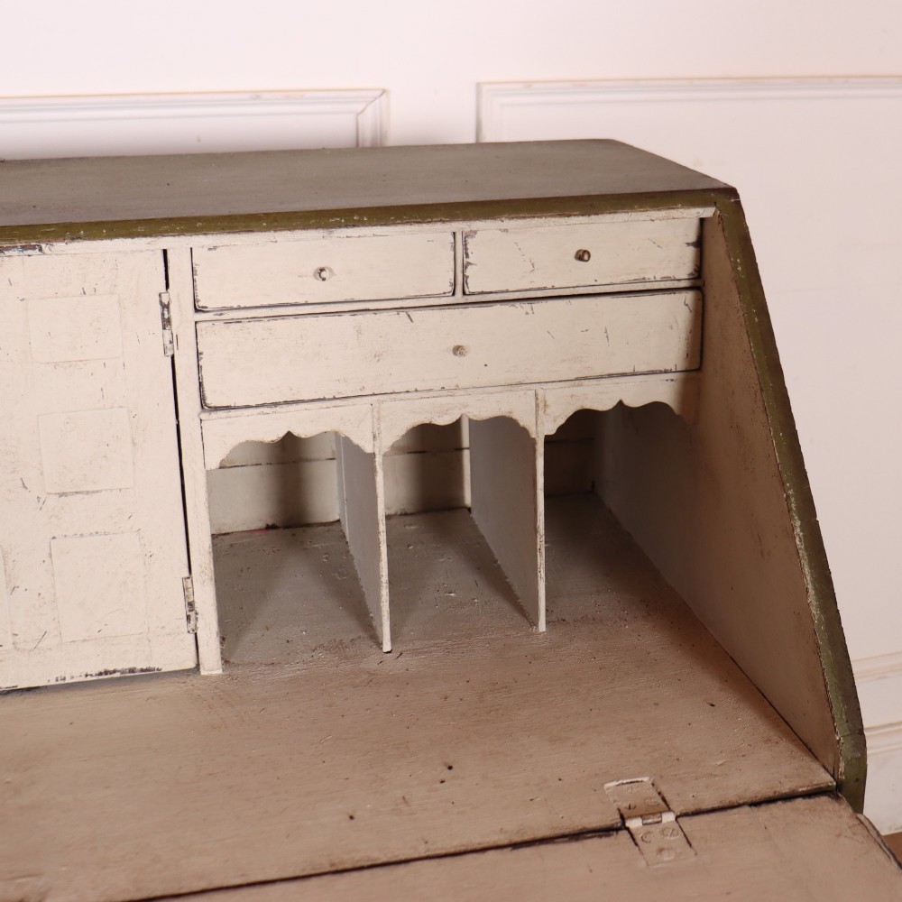 An antique English slant-front bureau with an olive green painted finish, brass handles, keyhole escutcheons, and four drawers resting on bracket feet. View VIII