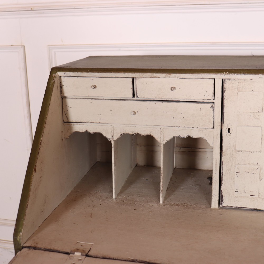 An antique English slant-front bureau with an olive green painted finish, brass handles, keyhole escutcheons, and four drawers resting on bracket feet. View X