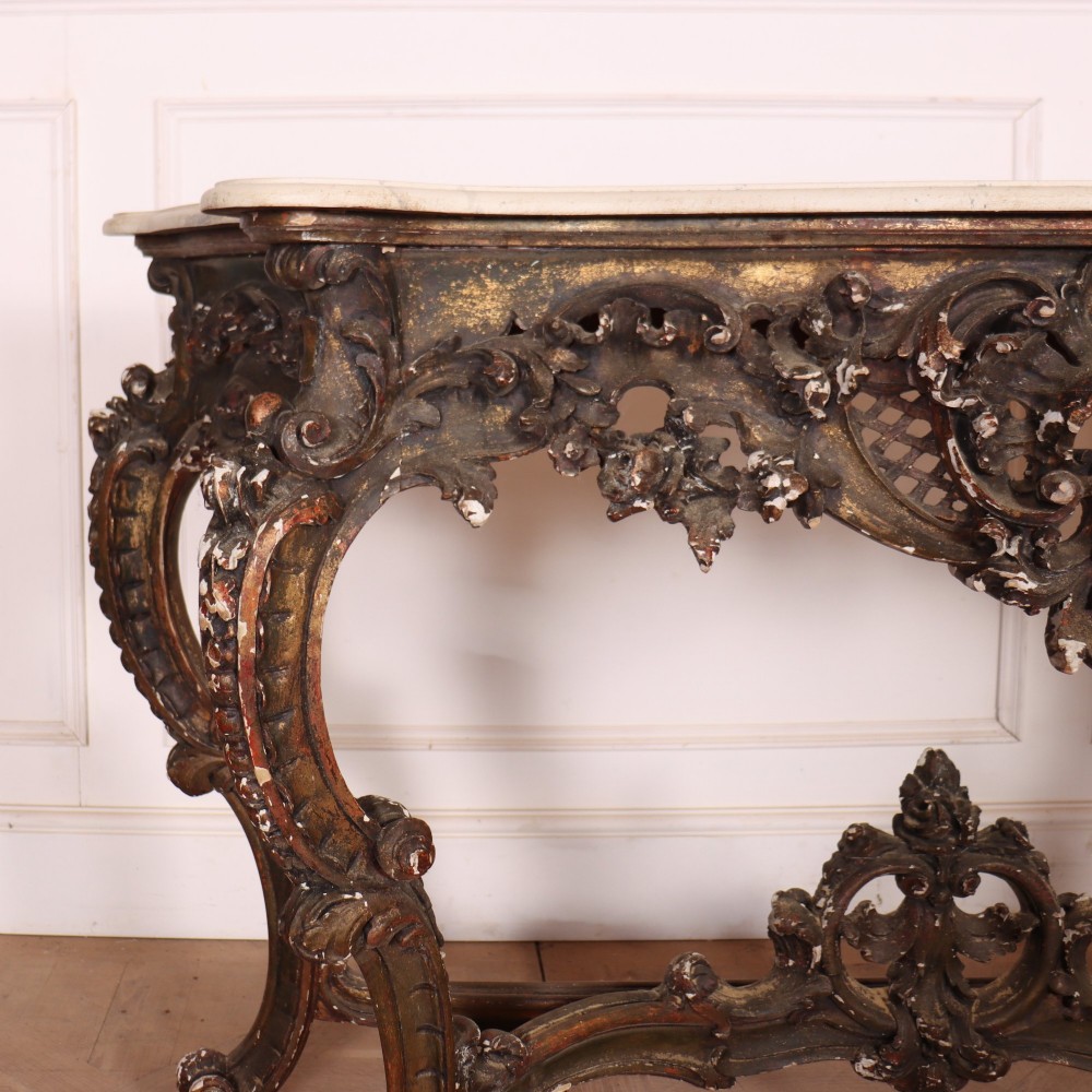 An antique French Rococo style console table featuring a cream marble top, elaborate rocaille carved giltwood apron, cabriole legs, and a decorative central stretcher. View II