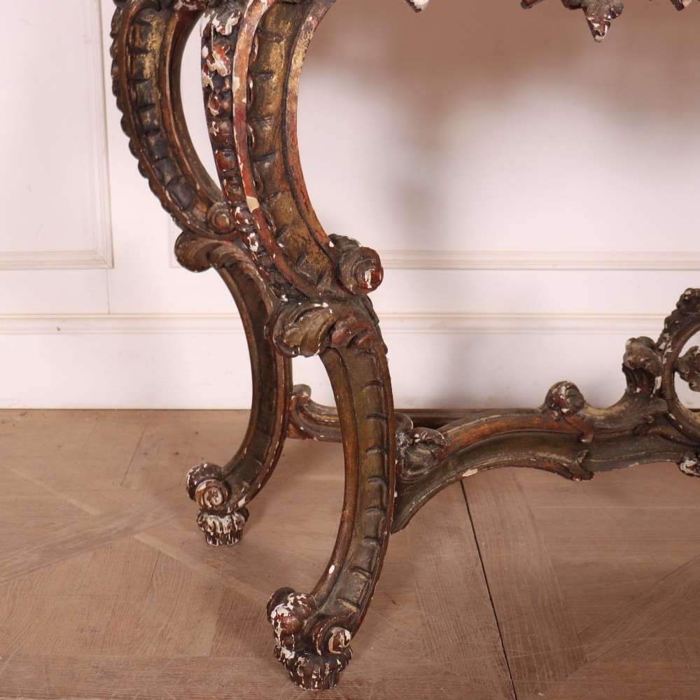 An antique French Rococo style console table featuring a cream marble top, elaborate rocaille carved giltwood apron, cabriole legs, and a decorative central stretcher. View III