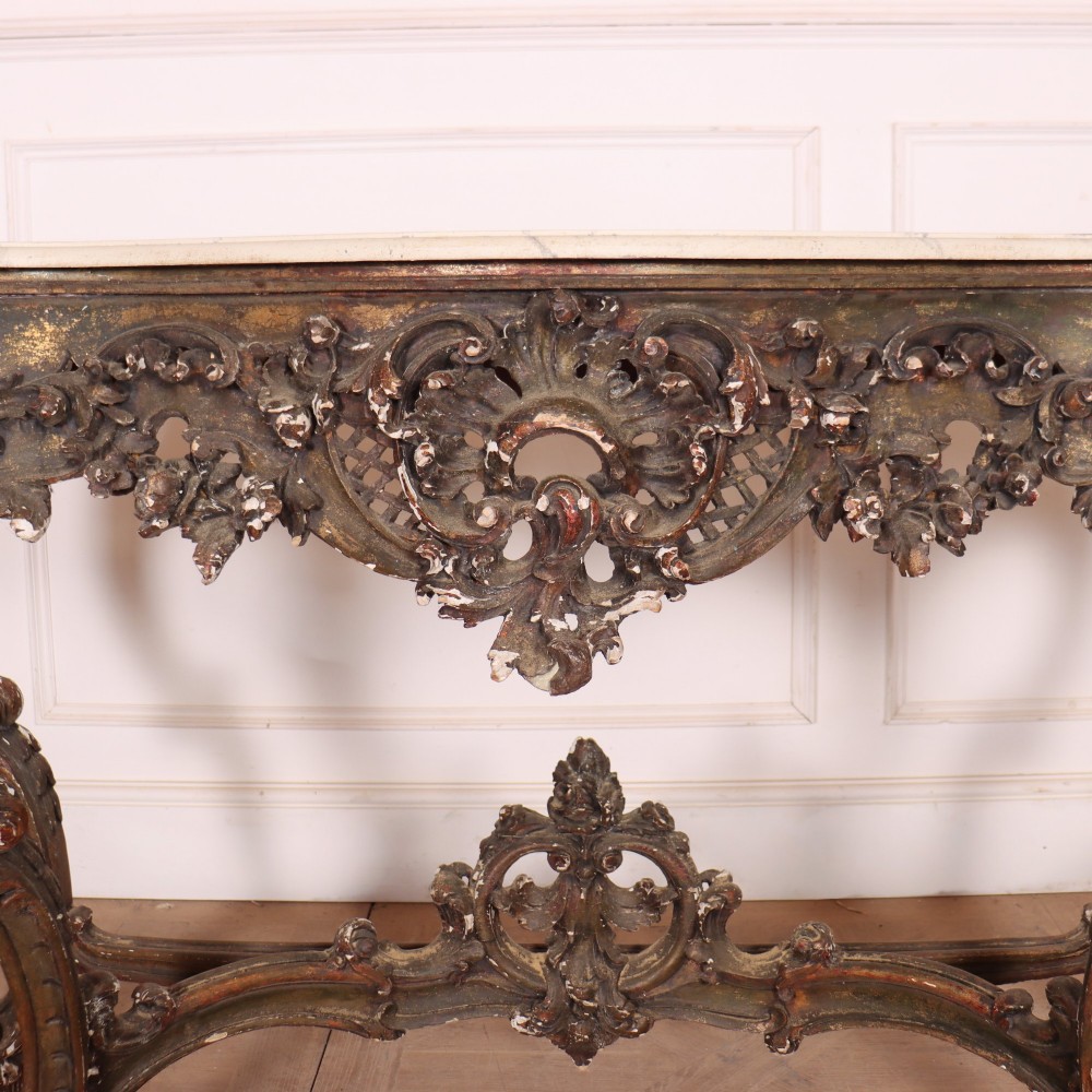 An antique French Rococo style console table featuring a cream marble top, elaborate rocaille carved giltwood apron, cabriole legs, and a decorative central stretcher. View IV