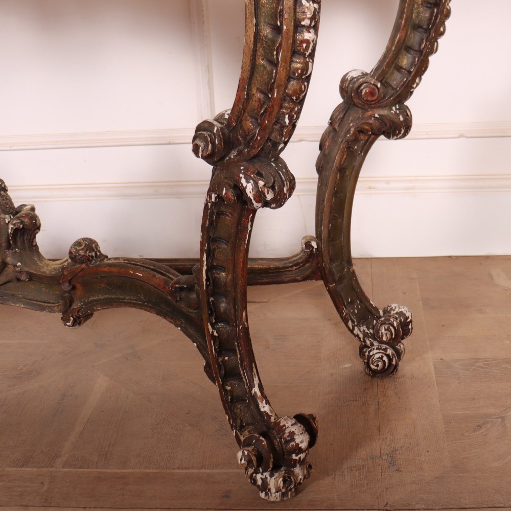 An antique French Rococo style console table featuring a cream marble top, elaborate rocaille carved giltwood apron, cabriole legs, and a decorative central stretcher. View VII