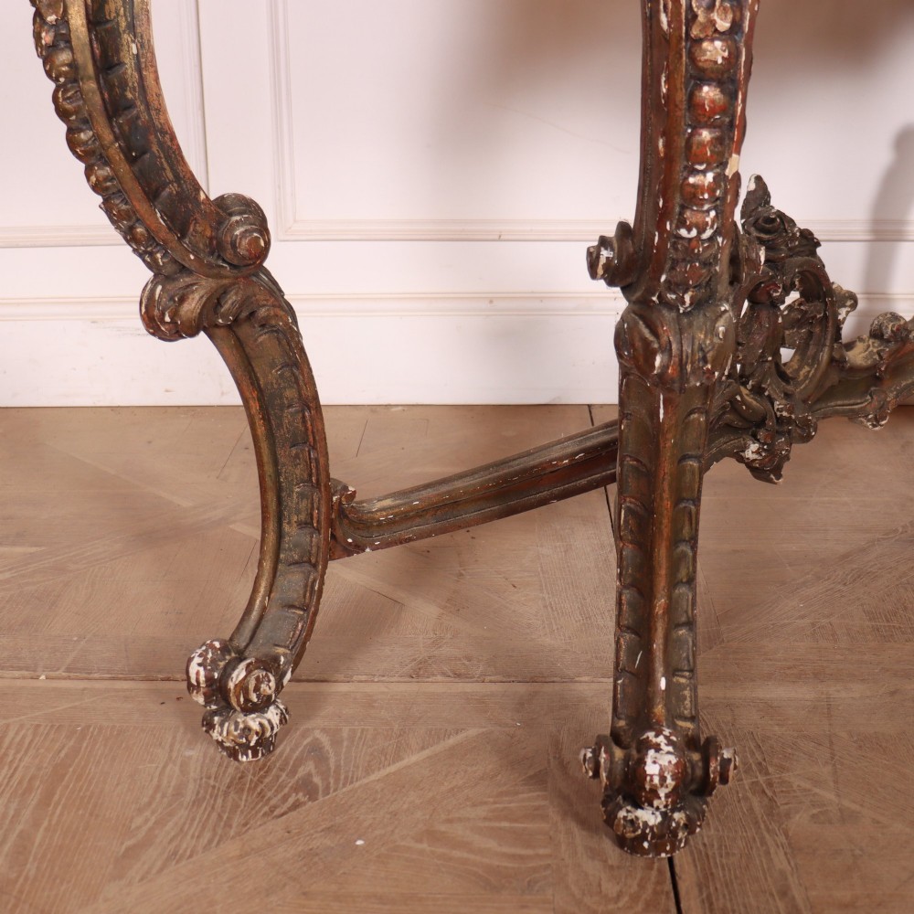 An antique French Rococo style console table featuring a cream marble top, elaborate rocaille carved giltwood apron, cabriole legs, and a decorative central stretcher. View X