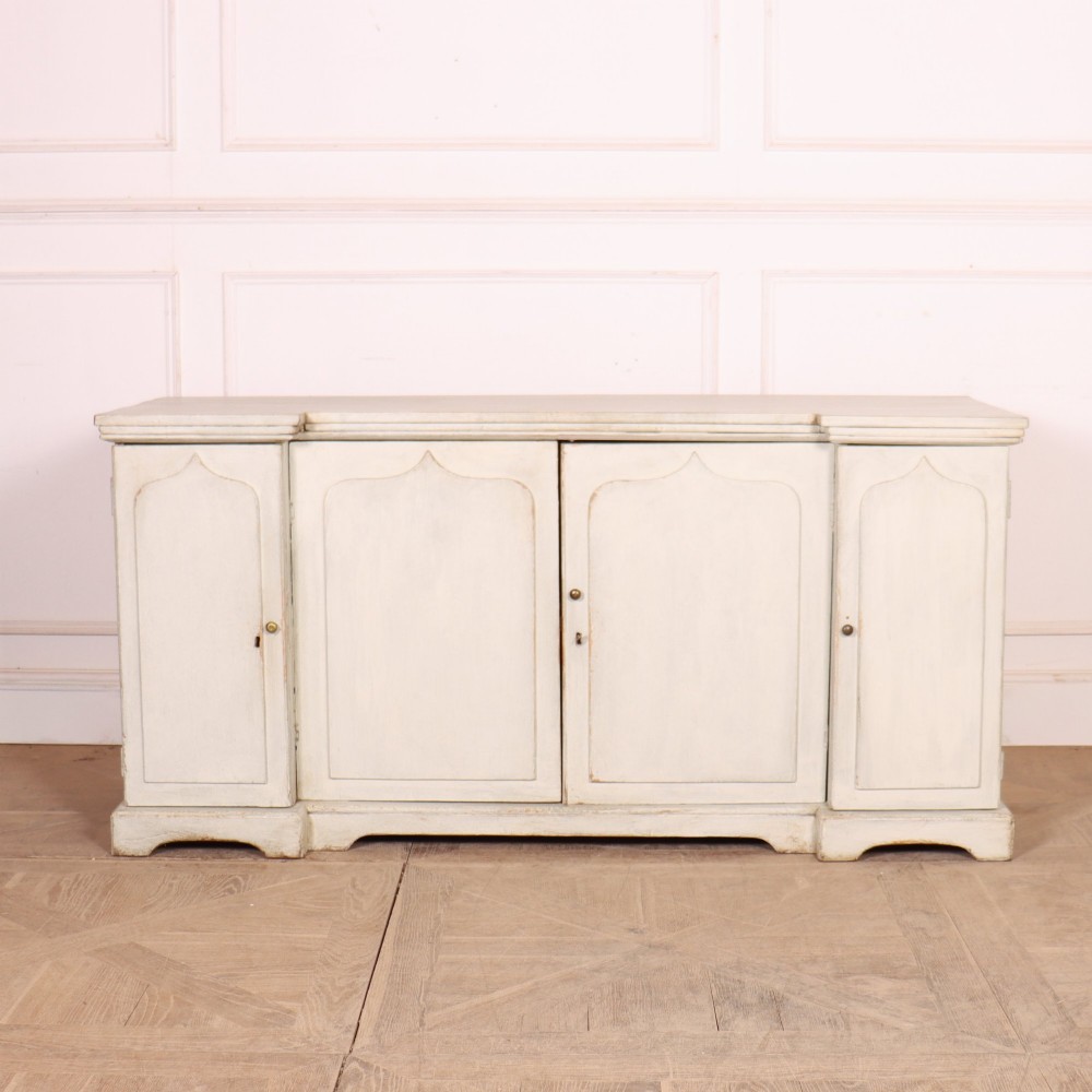 An off-white painted breakfront dresser base featuring four cupboard doors with arched panel mouldings and small brass knobs.