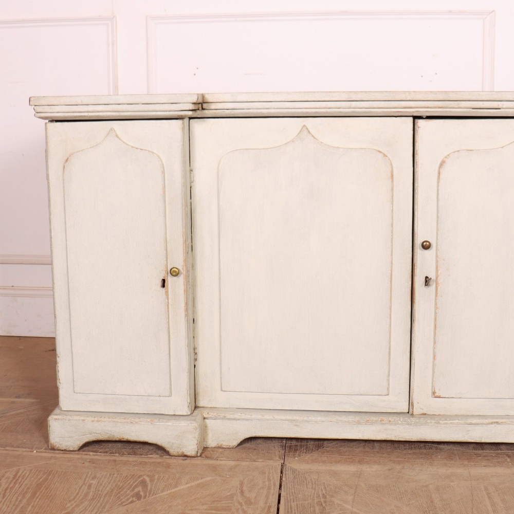 An off-white painted breakfront dresser base featuring four cupboard doors with arched panel mouldings and small brass knobs. View II