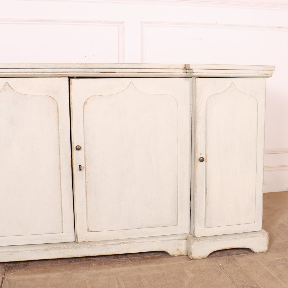 An off-white painted breakfront dresser base featuring four cupboard doors with arched panel mouldings and small brass knobs. View III