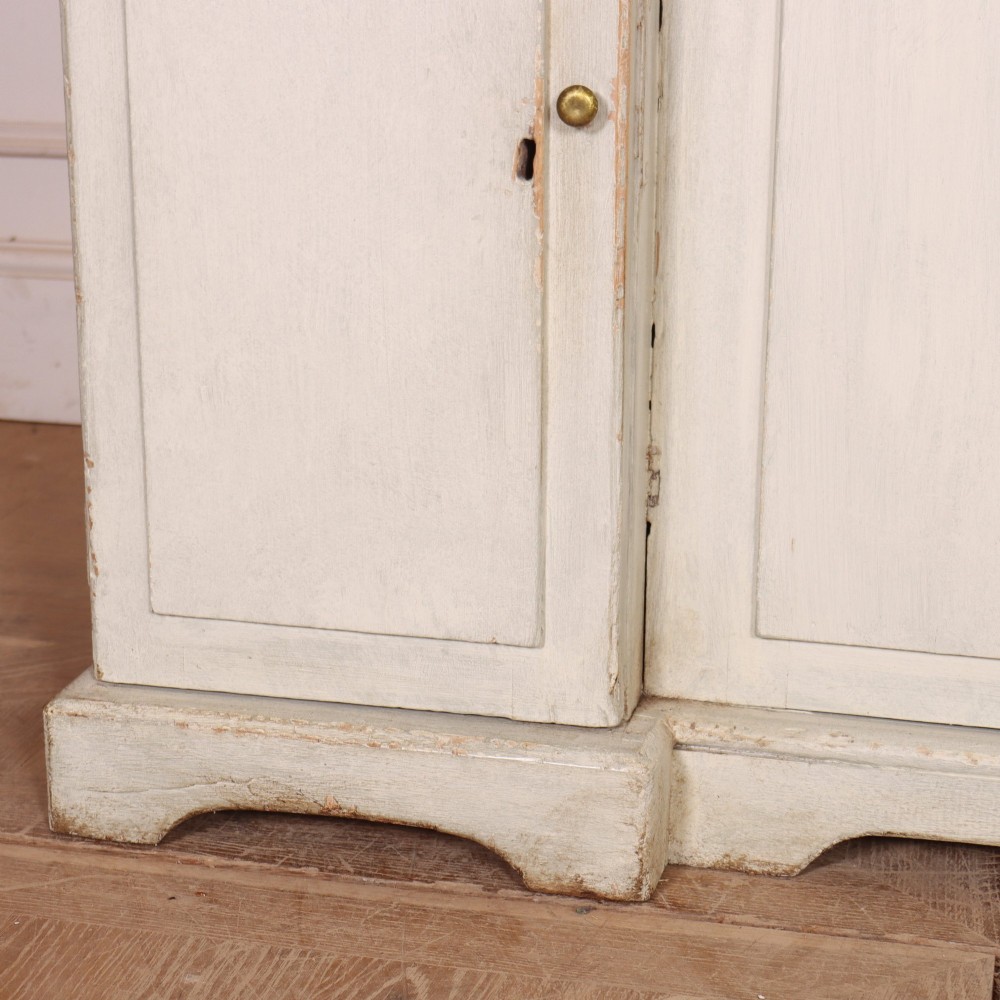 An off-white painted breakfront dresser base featuring four cupboard doors with arched panel mouldings and small brass knobs. View V