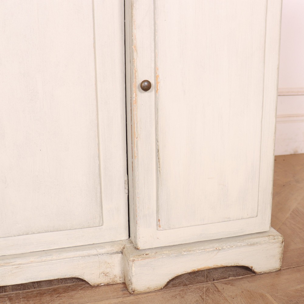 An off-white painted breakfront dresser base featuring four cupboard doors with arched panel mouldings and small brass knobs. View VII