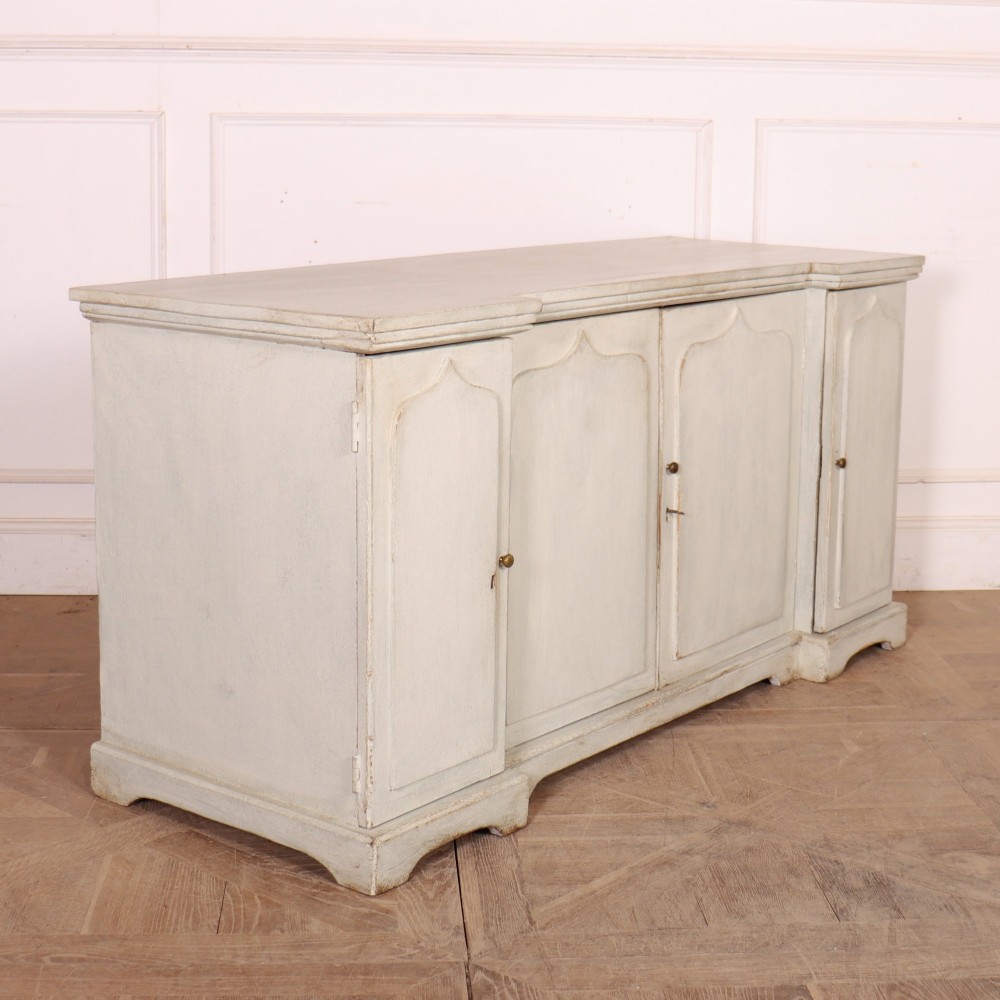 An off-white painted breakfront dresser base featuring four cupboard doors with arched panel mouldings and small brass knobs. View X