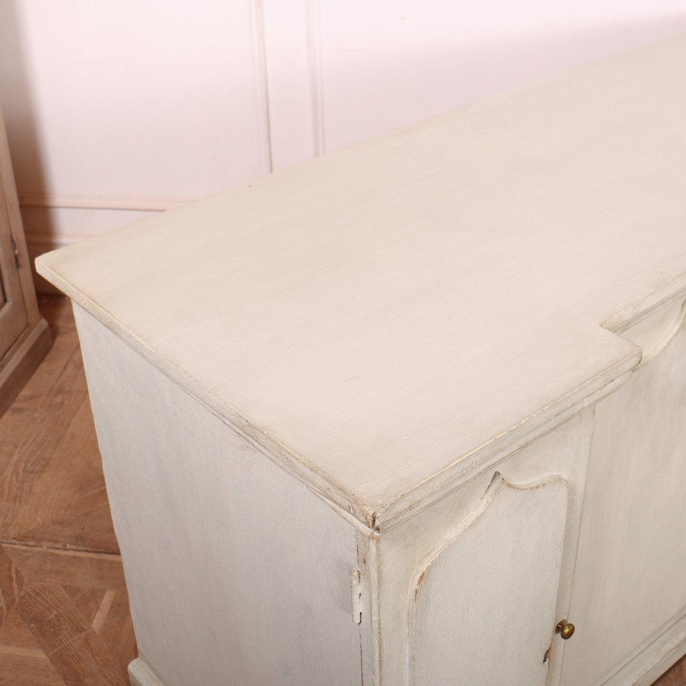 An off-white painted breakfront dresser base featuring four cupboard doors with arched panel mouldings and small brass knobs. View XI