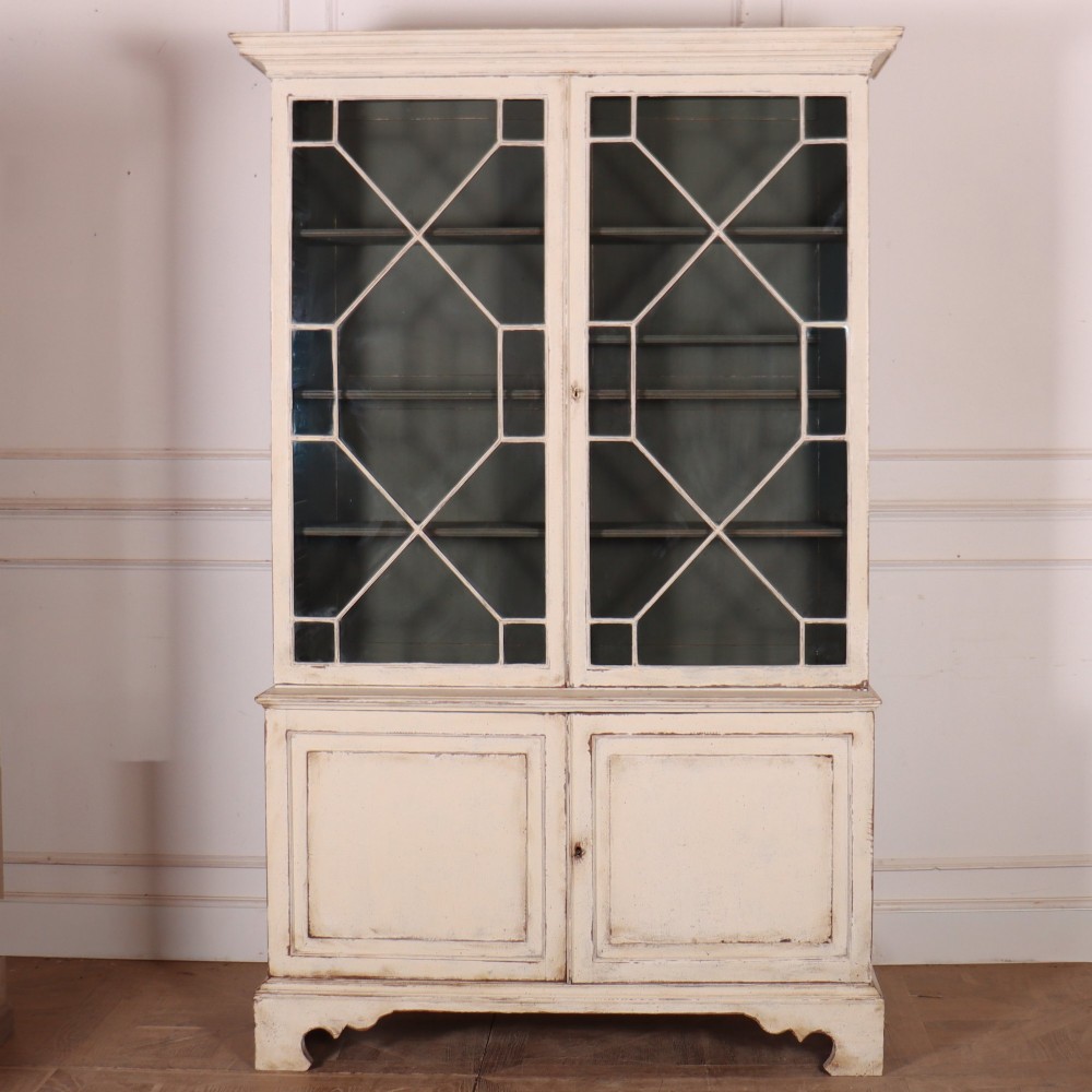 A cream painted English glazed bookcase featuring upper doors with geometric astragal glazing bars above a solid two-door cupboard base.