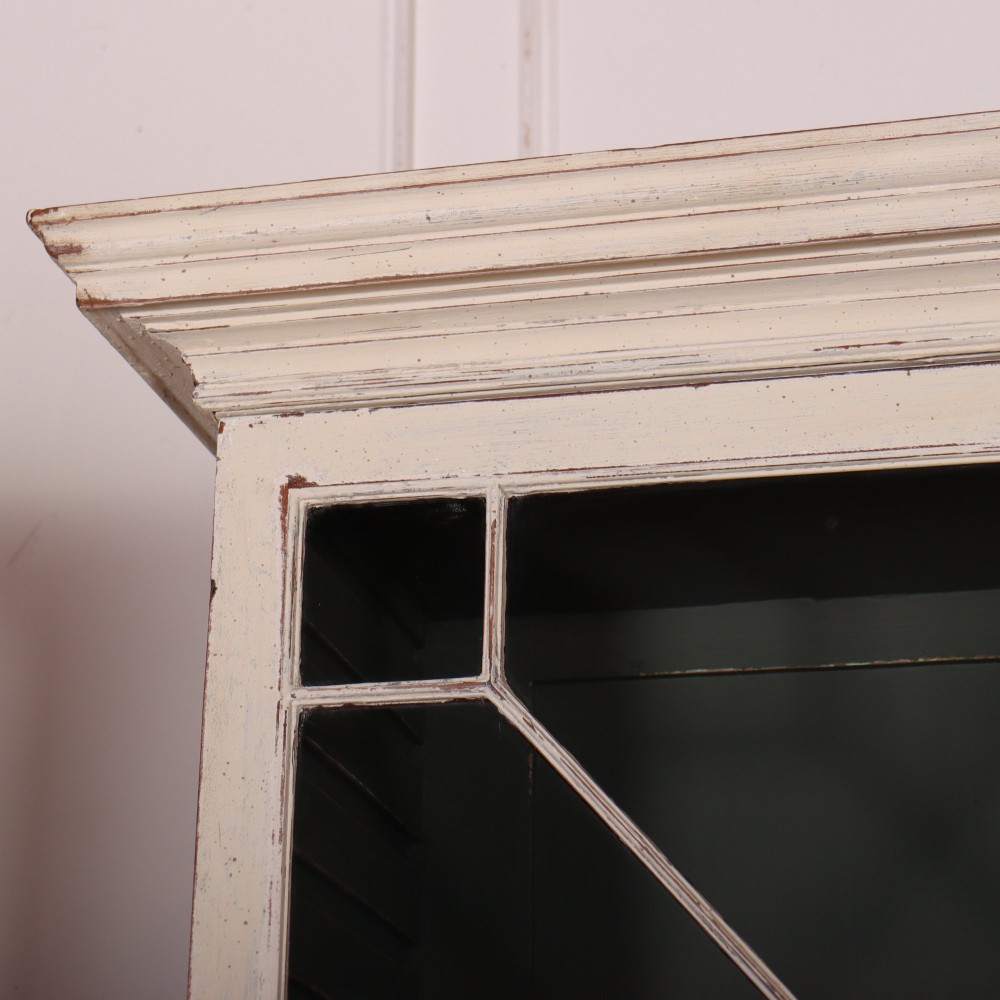 A cream painted English glazed bookcase featuring upper doors with geometric astragal glazing bars above a solid two-door cupboard base. View II