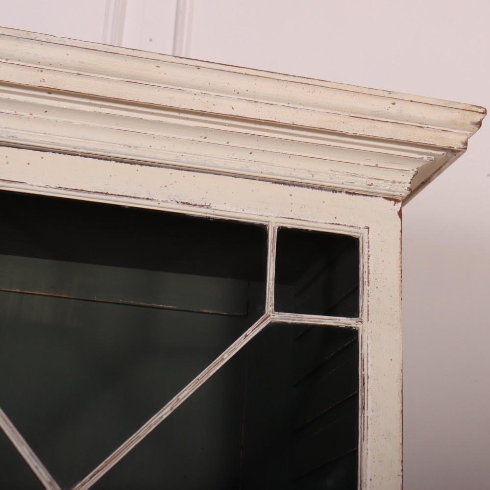 A cream painted English glazed bookcase featuring upper doors with geometric astragal glazing bars above a solid two-door cupboard base. View III