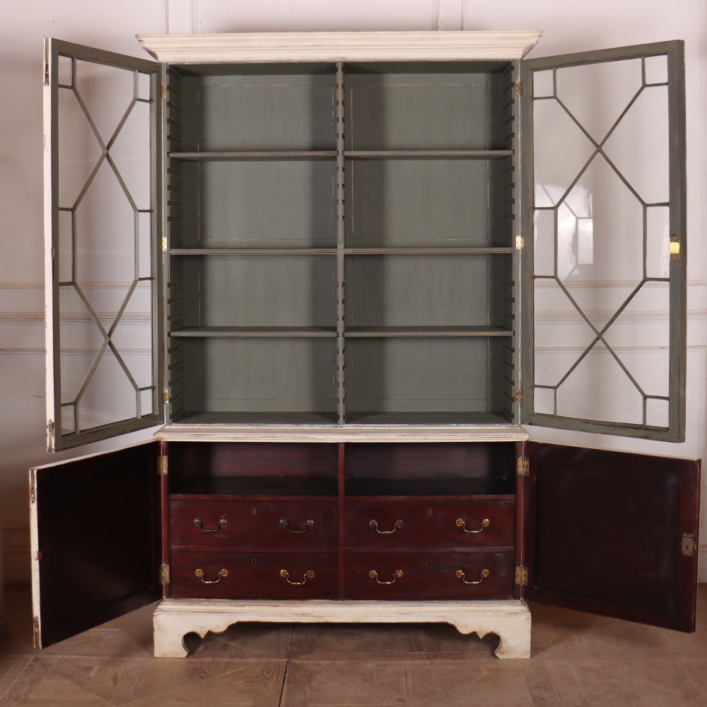 A cream painted English glazed bookcase featuring upper doors with geometric astragal glazing bars above a solid two-door cupboard base. View VIII