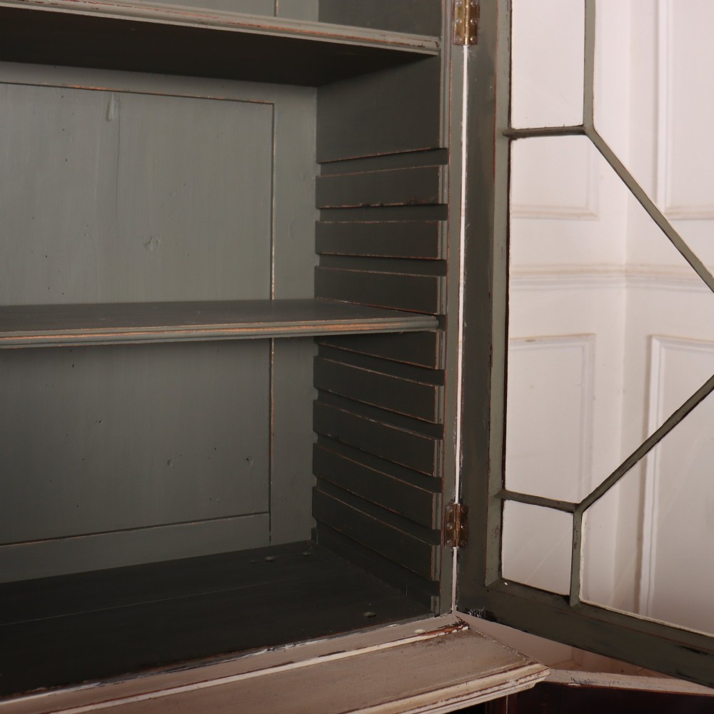 A cream painted English glazed bookcase featuring upper doors with geometric astragal glazing bars above a solid two-door cupboard base. View IX