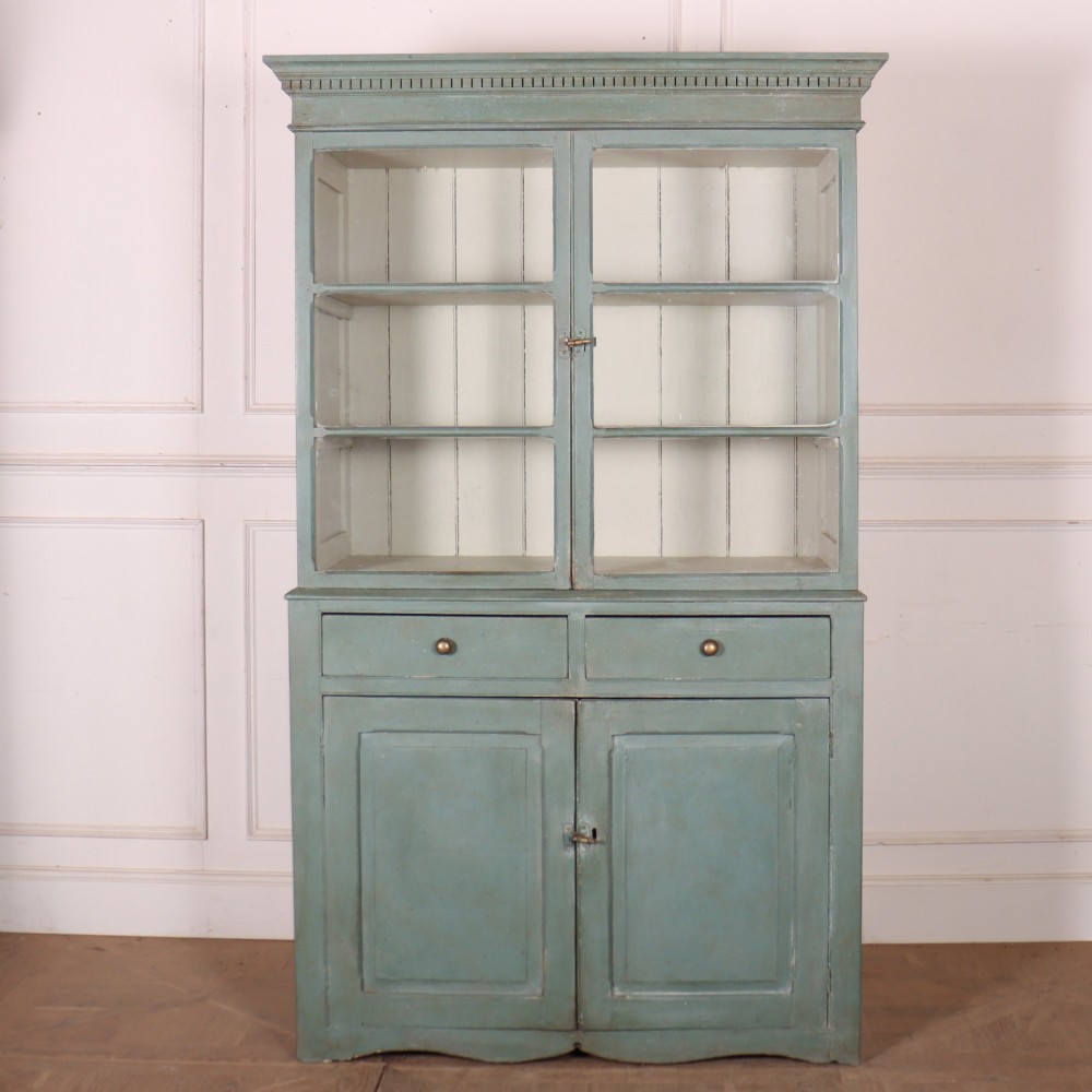 A tall two-part painted muted blue wood cabinet featuring an upper section with two glazed glass doors over a lower cupboard base with two drawers and panelled doors.