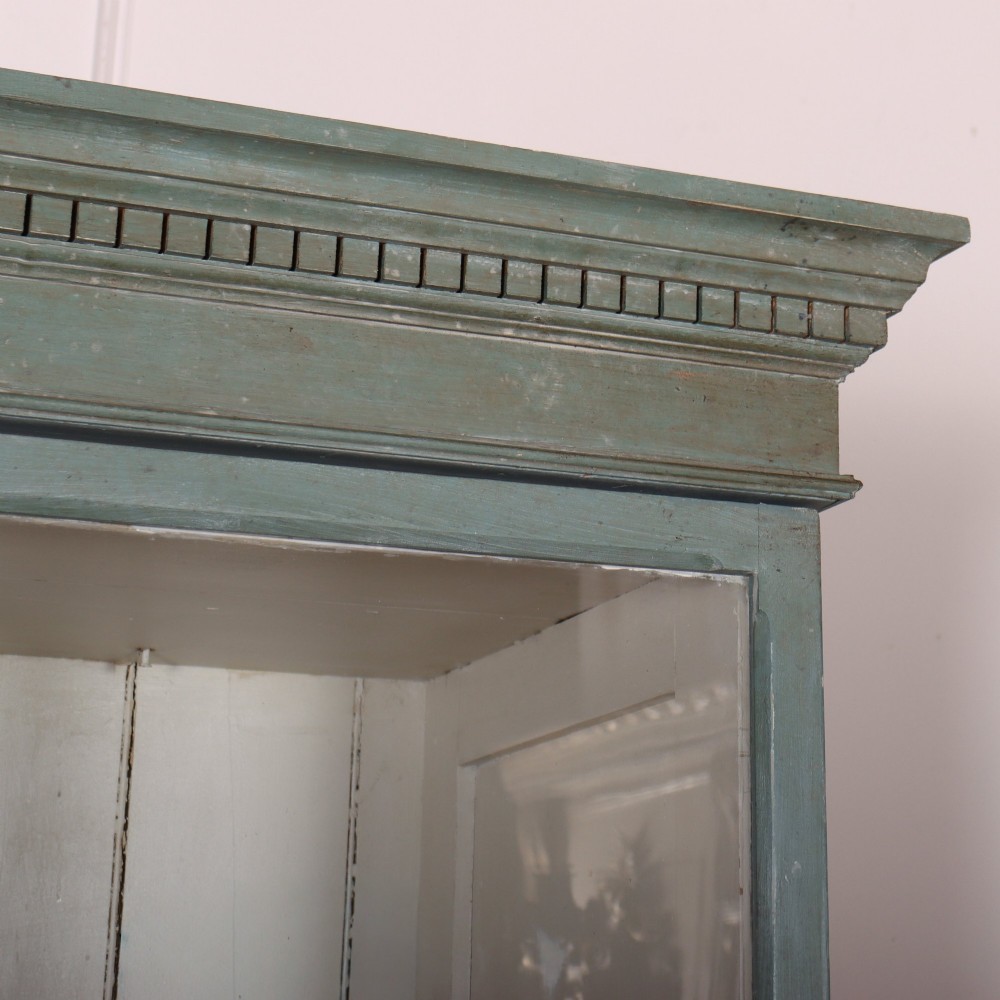 A tall two-part painted muted blue wood cabinet featuring an upper section with two glazed glass doors over a lower cupboard base with two drawers and panelled doors. View III