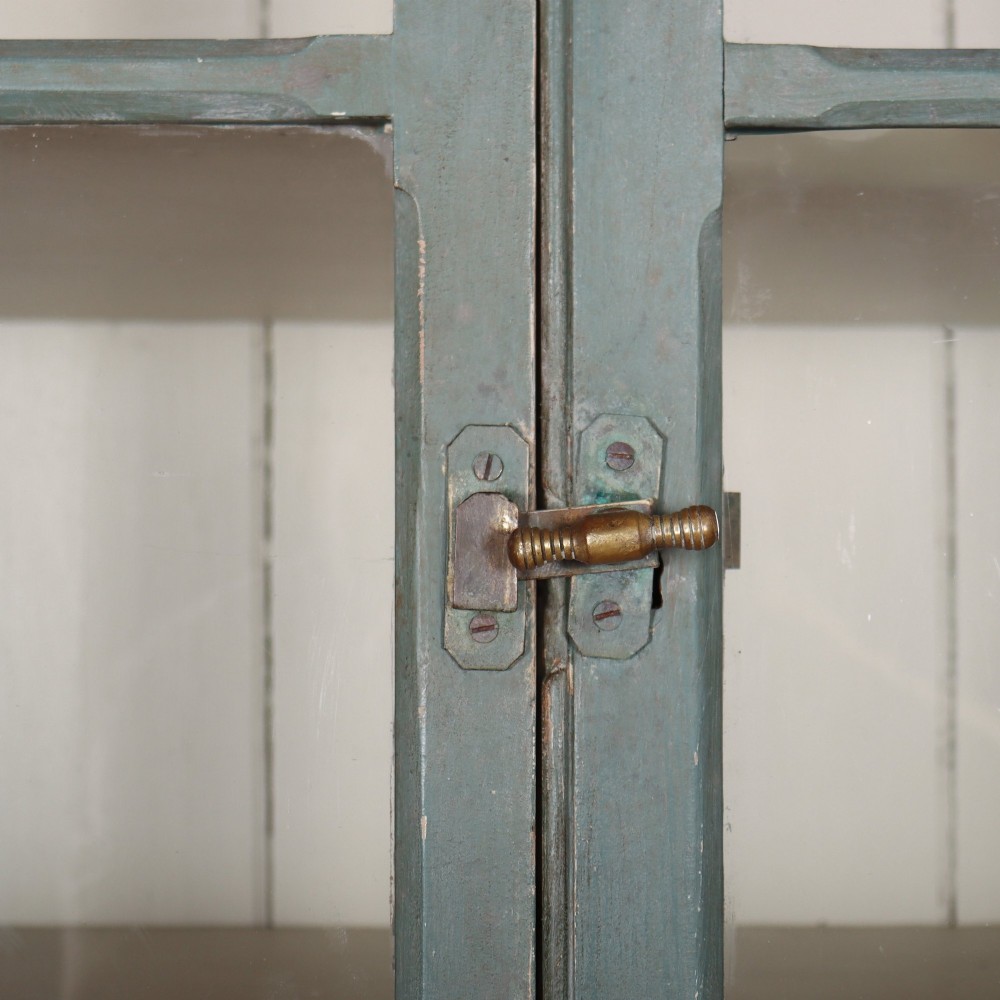 A tall two-part painted muted blue wood cabinet featuring an upper section with two glazed glass doors over a lower cupboard base with two drawers and panelled doors. View IV