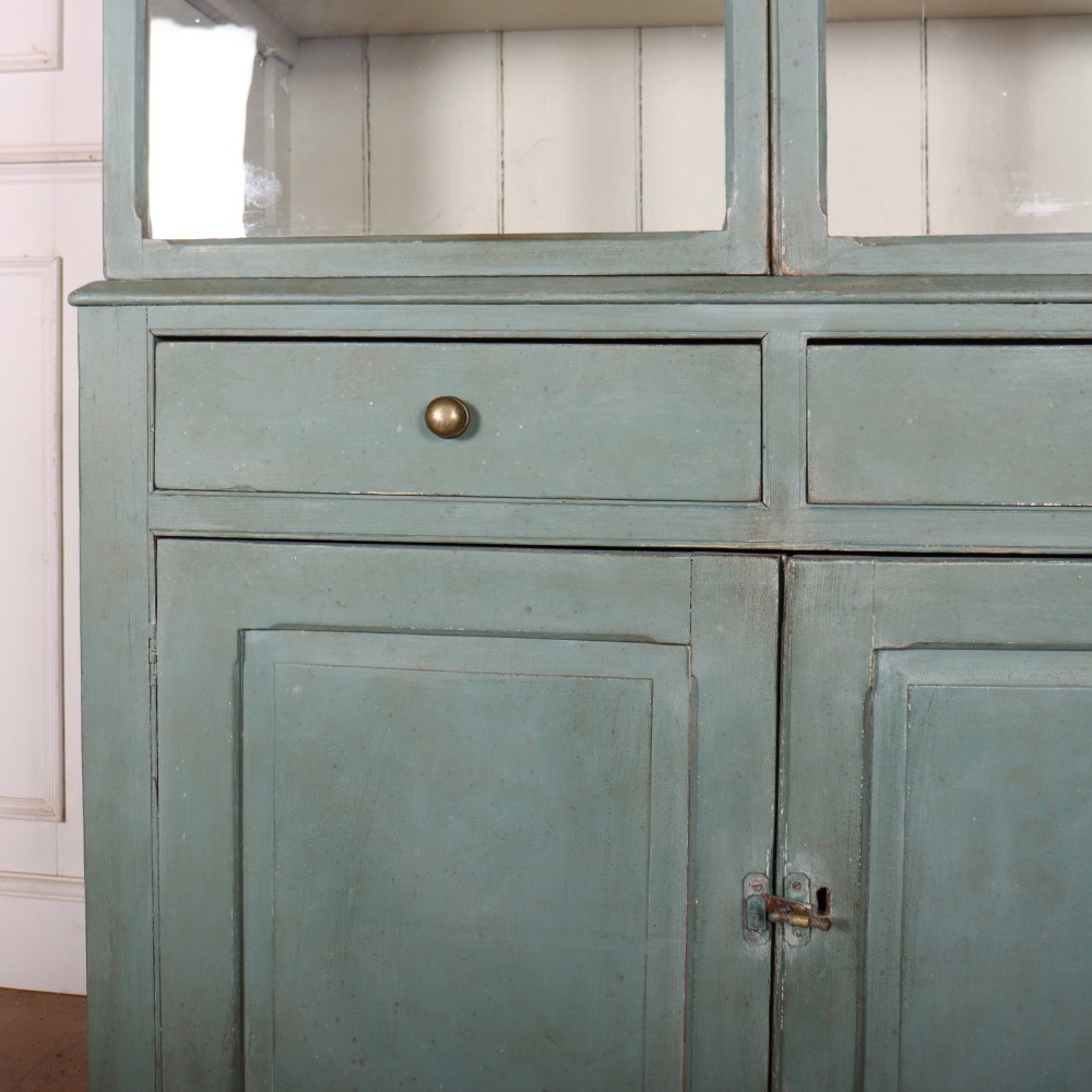 A tall two-part painted muted blue wood cabinet featuring an upper section with two glazed glass doors over a lower cupboard base with two drawers and panelled doors. View V