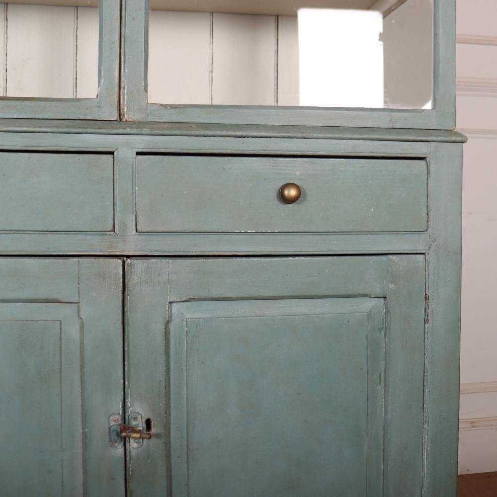 A tall two-part painted muted blue wood cabinet featuring an upper section with two glazed glass doors over a lower cupboard base with two drawers and panelled doors. View VI