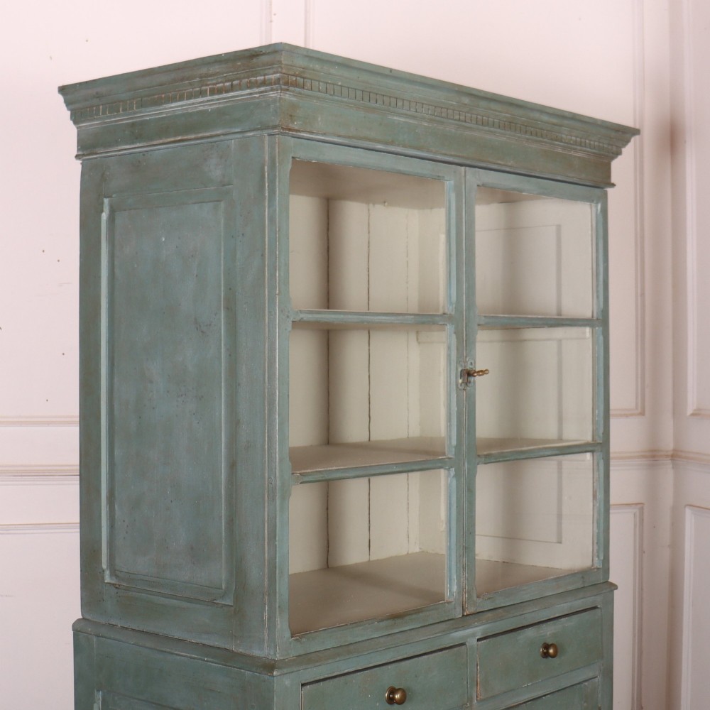 A tall two-part painted muted blue wood cabinet featuring an upper section with two glazed glass doors over a lower cupboard base with two drawers and panelled doors. View XI