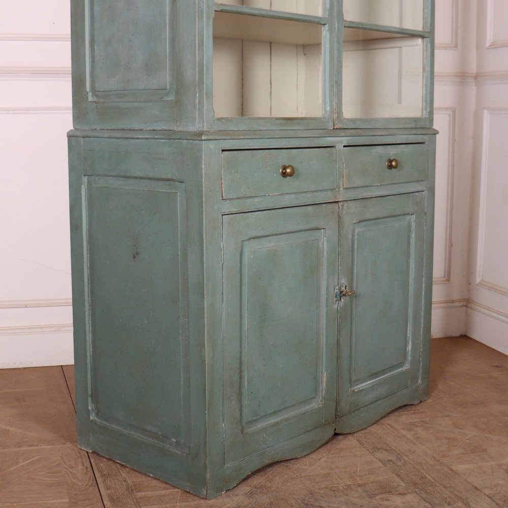 A tall two-part painted muted blue wood cabinet featuring an upper section with two glazed glass doors over a lower cupboard base with two drawers and panelled doors. View XII