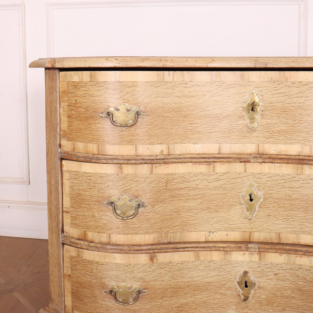 An Austrian bleached oak commode featuring a serpentine front, three drawers with crossbanded borders, brass escutcheons, handles, and turned feet. View II