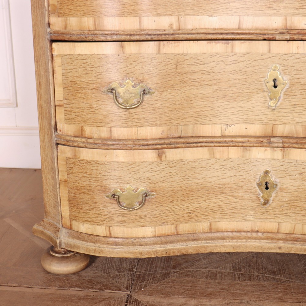 An Austrian bleached oak commode featuring a serpentine front, three drawers with crossbanded borders, brass escutcheons, handles, and turned feet. View III