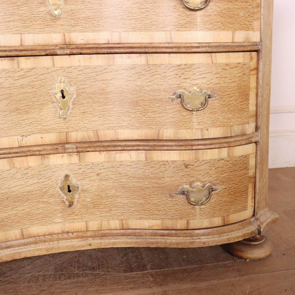 An Austrian bleached oak commode featuring a serpentine front, three drawers with crossbanded borders, brass escutcheons, handles, and turned feet. View IV