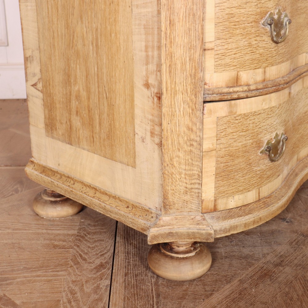 An Austrian bleached oak commode featuring a serpentine front, three drawers with crossbanded borders, brass escutcheons, handles, and turned feet. View VIII